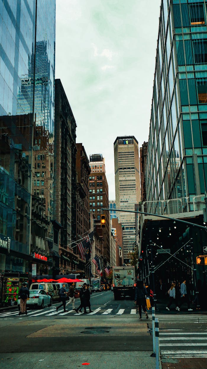 Urban street scene with skyscrapers and people under cloudy sky, portraying city life.