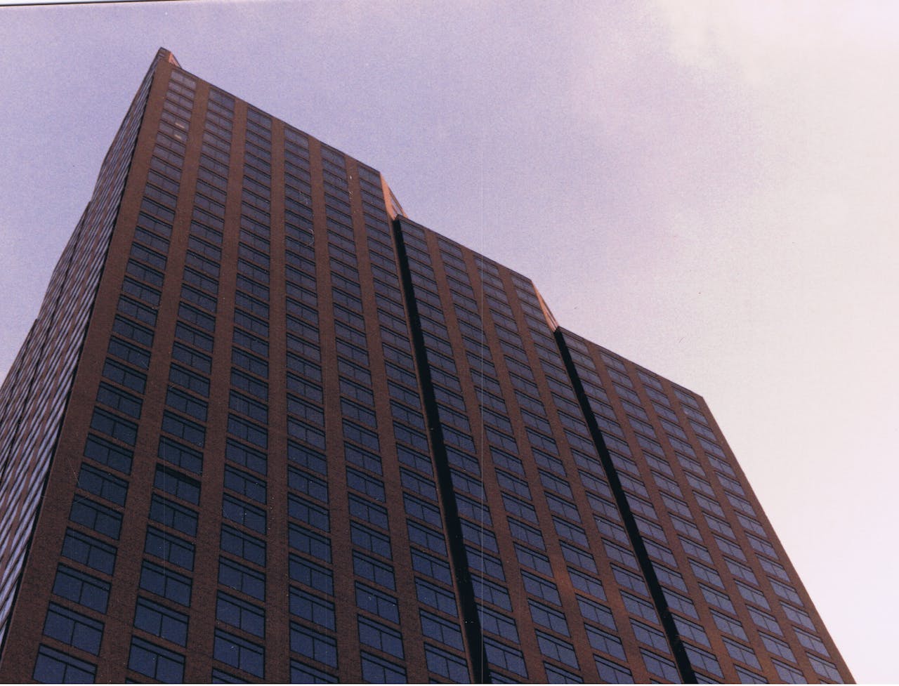 Low-angle view of a tall modern skyscraper with symmetrical window patterns against a cloudy sky.